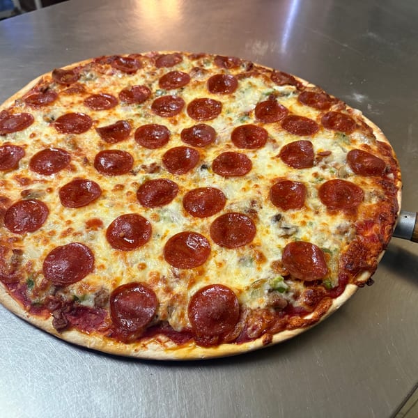 Freshly baked pepperoni pizza with melted cheese, green peppers, and sausage on a metal counter.