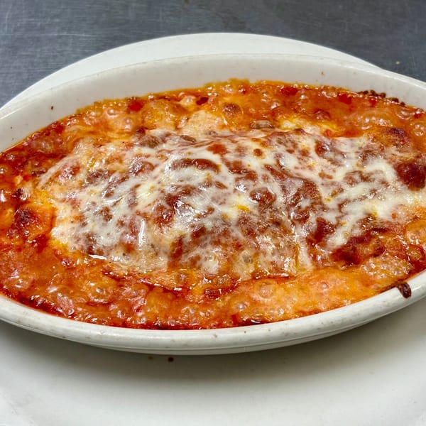 Baked lasagna with bubbly melted cheese and red sauce in a white oval dish.