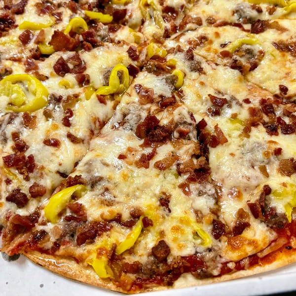 Close-up of a pizza topped with melted cheese, bacon, ground meat, and yellow peppers.