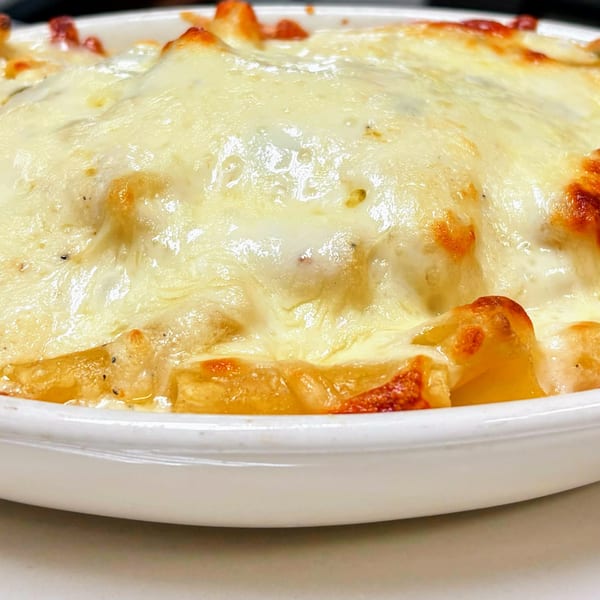 Close-up of a white oval dish filled with baked ziti pasta, topped with melted, bubbly cheese.