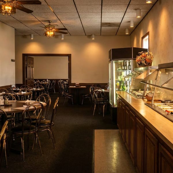 An empty restaurant dining room with tables, chairs, and a buffet line with fresh salad ingredients.