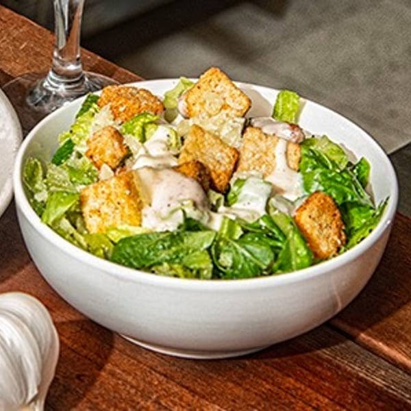 A white bowl filled with Caesar salad, featuring crisp lettuce, croutons, and creamy dressing.