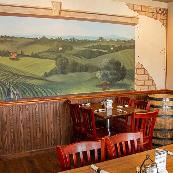 Restaurant dining area with wooden tables and chairs, featuring a large mural of a vineyard landscape.