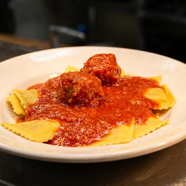 Ravioli pasta topped with two meatballs and red marinara sauce on a white plate.
