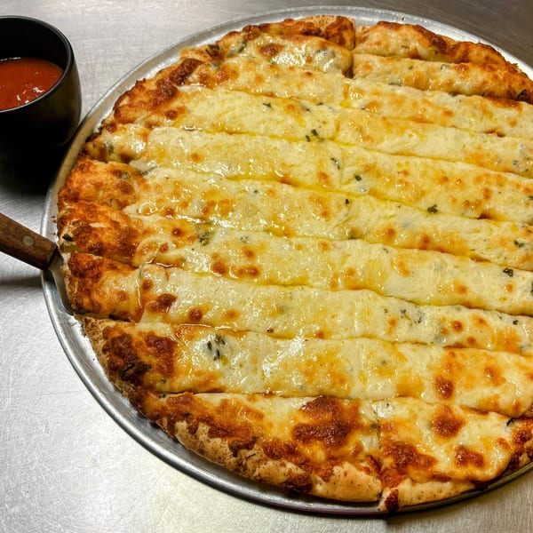 Cheesy garlic breadsticks with a side of marinara sauce on a metal tray.